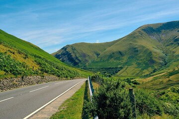 Landscape of a highway surrounded by hills and greenery under a blue sky and sunlight