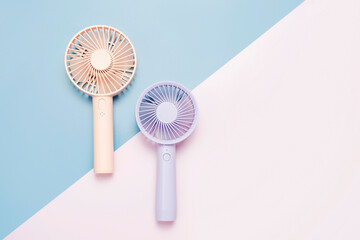 Small portable mini fans on blue and pink background close-up.