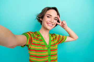 Photo of charming cute lady wear striped cardigan showing v-sign cover eye tacking selfie isolated teal color background
