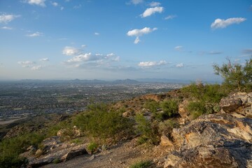 Rocky terrain near trees and a city with a few clouds in the sky, Phoenix, Arizona