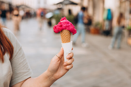 Colorful tasty ice cream cone in hand. Close up image of woman hand holding fresh waffle cone with pink ice cream Outdoors, food and rest concept