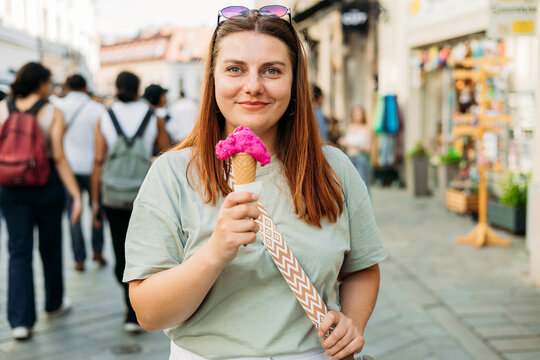 Colorful tasty ice cream cone in hand. Close up image of woman hand holding fresh waffle cone with pink ice cream Outdoors, food and rest concept