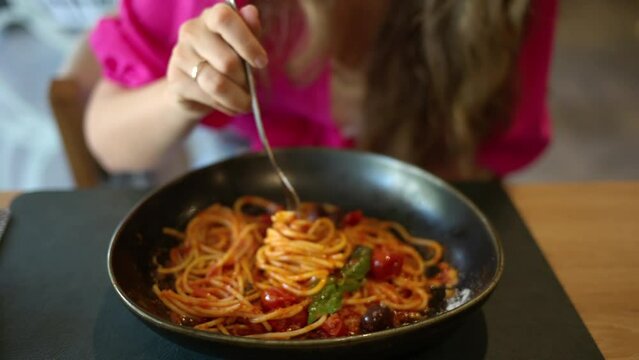 Woman eating italian spaghetti with tomatoe and basilic in a restaurant