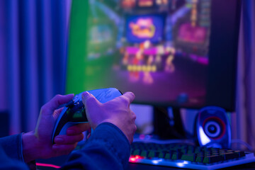 Selective focus at hand playing online game on computer monitor and smartphone with colorful gaming...