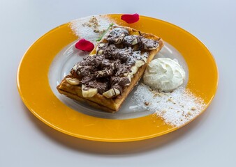 Close-up of a plate with a freshly-made waffle topped with a swirl of white whipped cream