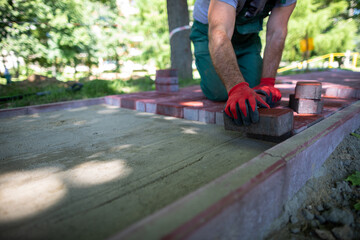 A skilled construction worker lays red paving stones on a sidewalk.