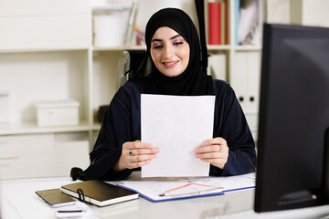Woman in Hijab Abaya working at office doing task work. On duty Emirati lady holding a paper with...