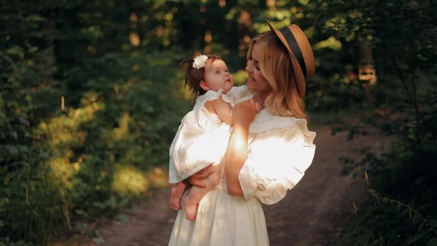 Young smiling mother holding and kissing her little newborn baby daughter while walking outdoors in the park. mother and child together