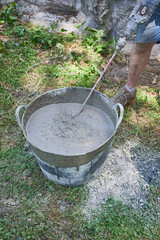 Unrecognizable worker mix cement with water using a drill tool. Buckets, mixer and powdered cement prepared to be used in a home repair.
