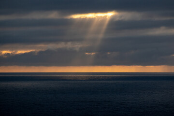 Sunlight shining through the cloud-covered sky onto the water in the middle of the ocean, SeaPoint, Cape Town 2/2