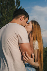 Fototapeta premium Young beautiful couple attractive boy and girl posing and kissing on a country field. Peace and freedom in nature