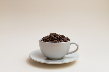 White cup filled with coffee beans isolated on cream background