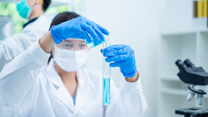Close up of female scientist or researcher is pouring blue substance or liquid into sample test...