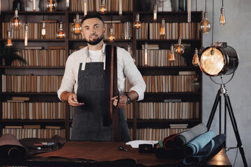 Portrait tailor man working with leather textile at his workshop. Craft manual production of waist belts, small business