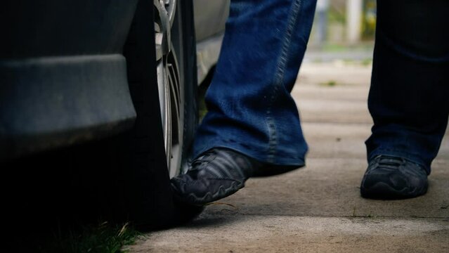 Angry car driver kicks flat tire on car 