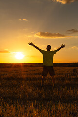 A man on his back with his arms open and outstretched in the middle of the field is watching and enjoying the sunset in the summer day. Vertical.