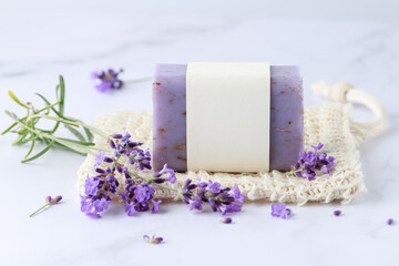 Aroma herbal handcraft soap with lavender flowers for bath relaxation and body care on sisal net bag over white marble table background. Home spa lifestyle. - obrazy, fototapety, plakaty