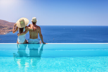 A couple hugging at the edge of an infinity pool and enjoying the view to the blue, mediterranean...