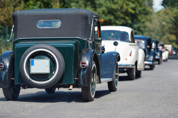 Row of old vintage cars driving down the road on sunny day, view form behind