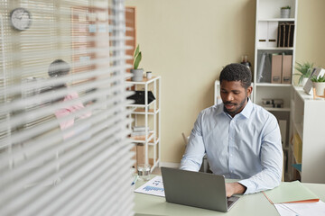Portrait of adult African American man working with laptop at desk in office, copy space