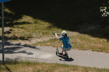 Obraz premium warsaw, poland - 31 07 2023: A small child in a plaid shirt going on the pavement on a scooter
