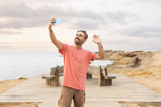 Man taking selfie on beach at sunset smiling looking at camera