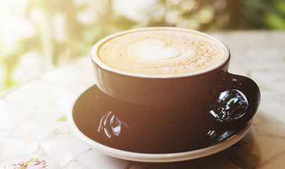 Coffee in black cup on table in cafe with lighting background