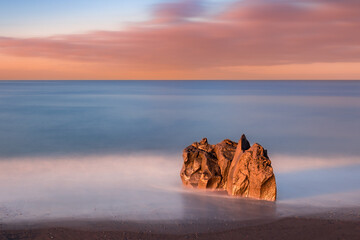Minimalist long exposure seascape in morning at sunrise with lone rock and blurred milky water