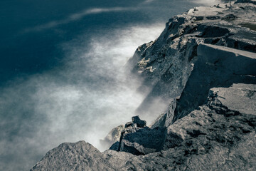 Artistic seascape with blurry waves crashing against granite rocks on shore at sunny day, Madeira