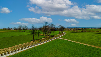 Obraz premium A Drone View of a Single Rail Road Track, Going Around a Curve, Thru Green Farmlands on a Blue Sky, With Clouds Day