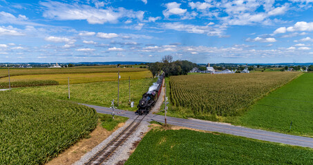 A Drone Frontal View of a Restored Steam Passenger Train, Traveling Thru Green Corn Fields, Blowing...