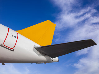 Yellow-tailed plane. The rear of the passenger plane, detail from the stern, a yellow tail and an azure cloudy sky. An airplane photo taken from the bottom. vibrant colors