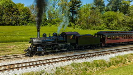 An Aerial View from the Side of An Antique Steam Locomotive and Passenger Coach Stopped and Blowing Smoke and Steam, While Waiting for Passengers to Board on a Sunny Spring Day