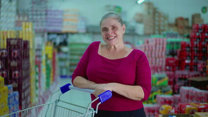 Cheerful Middle-Aged Woman in Supermarket Aisle with Shopping Cart, depicting consumerism lifestyle habits