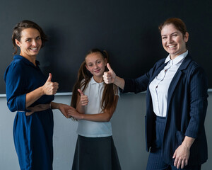 The teacher and the mother of the schoolgirl stand at the blackboard and show a thumbs up. 