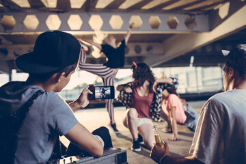 Group of young people break dancing in a parking lot and recording with their smart phone