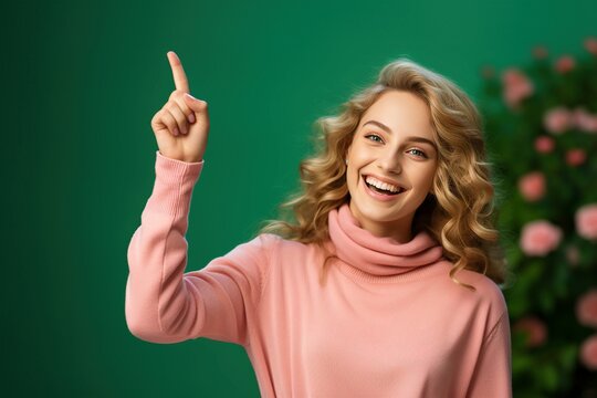 Pretty young woman raising index finger, very happy, pink top, green background, isolated