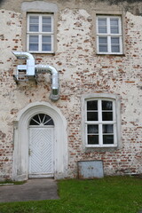 Fototapeta na wymiar moderne Abluftrohre auf unverputzter alter Ziegelwand mit halbrunder Haustüre
