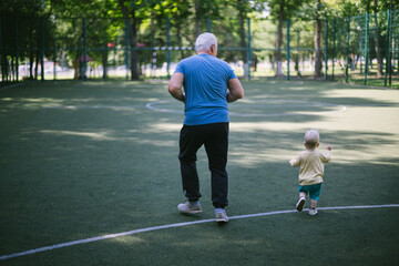 Obraz premium a gray-haired senior man 50 years old runs with his grandson in a race in the park on the sports ground