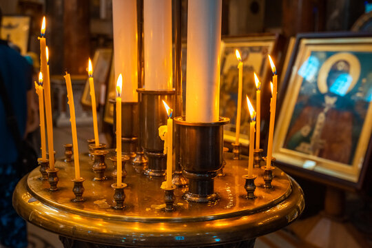 Burning Candles On The Altar Opposite The Faces Of The Saints In The Church Hall.