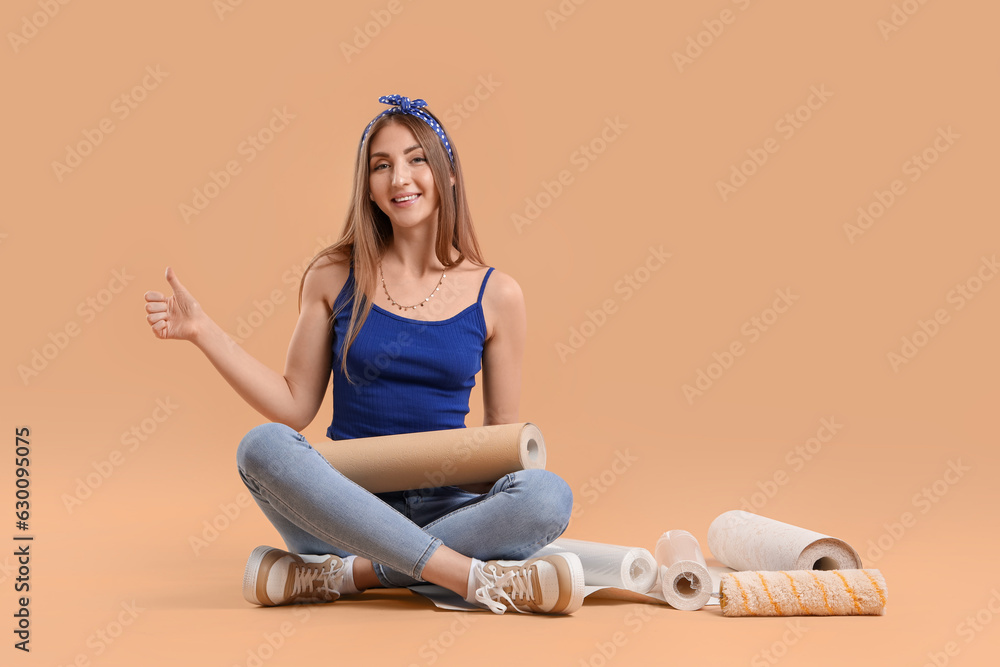 Wall mural Young woman with wallpaper roll showing thumb-up on beige background