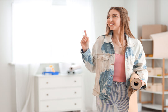 Young woman with wallpaper roll pointing at something in room