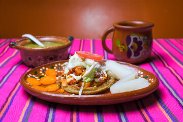 sopes accompanied by green sauce and coffee in a clay dish on a colorful background