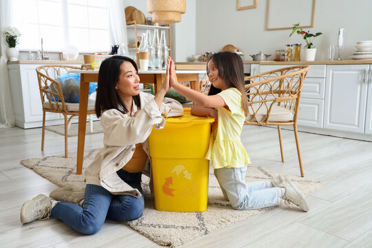 Asian mother with her little daughter and recycle bin giving each other high-five in kitchen