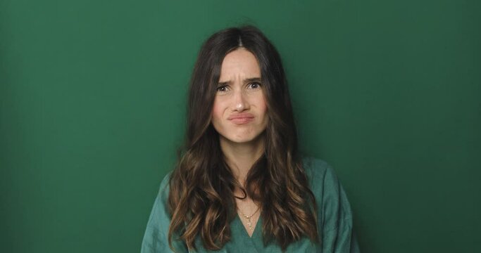 Annoyed and bored brunette woman cant stand it anymore, making finger pistol, gun gesture and shooting herself at head from irritation and boredom, standing green background