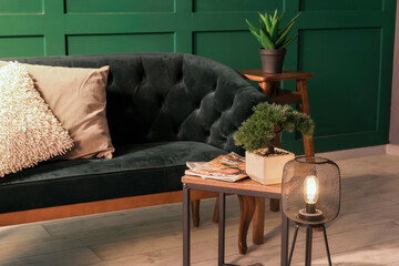 Interior of dark living room with green sofa, coffee table and glowing lamp