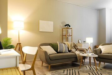 Interior of living room with grey sofa, armchair and glowing lamps