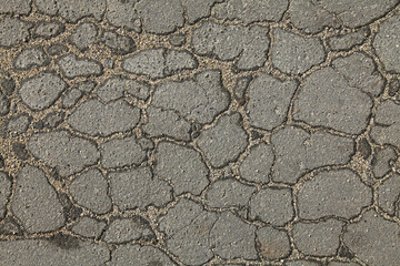Asphalt surface of the road with a cracks in the middle, background. Web of cracks. Textured backdrop. Detailed texture of the bitumen close-up. Soviet road without repairs