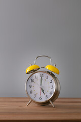 Retro silver alarm clock. 5:00.  am,  pm. Neutral background. Brown wood surface. Vertical photography with empty space for text or image.