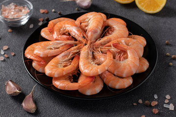 Boiled shrimps in a black plate and spices on dark gray background
